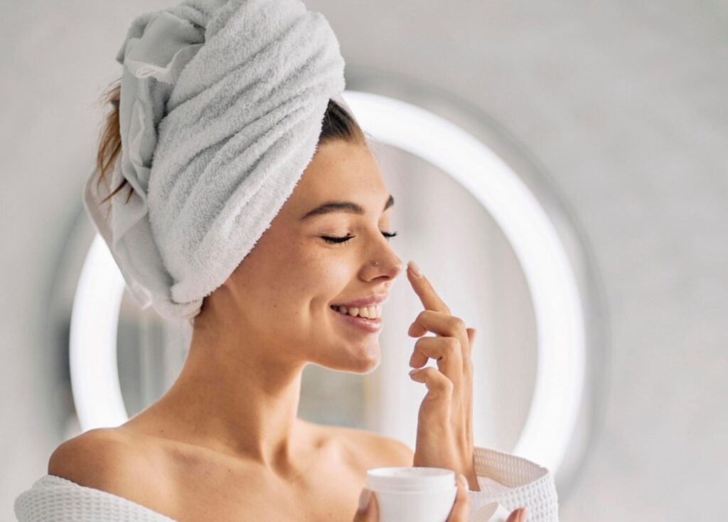 Lächelnde Frau beim Pflegeritual im Badezimmer – Symbol für achtsame Hautpflege und Selbstachtung